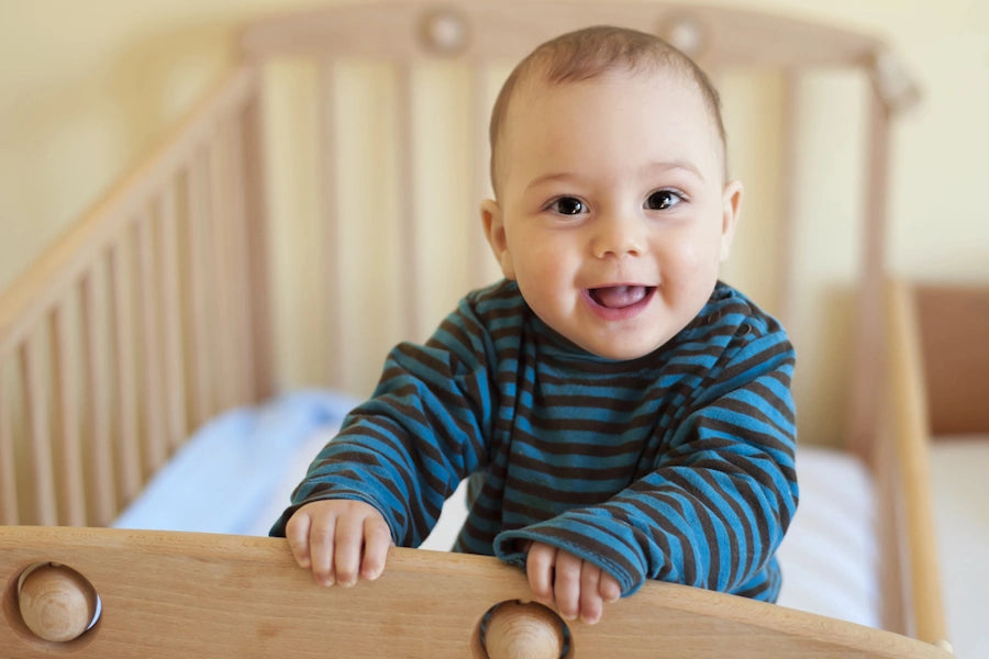 Un bébé souriant dans son lit en bois.